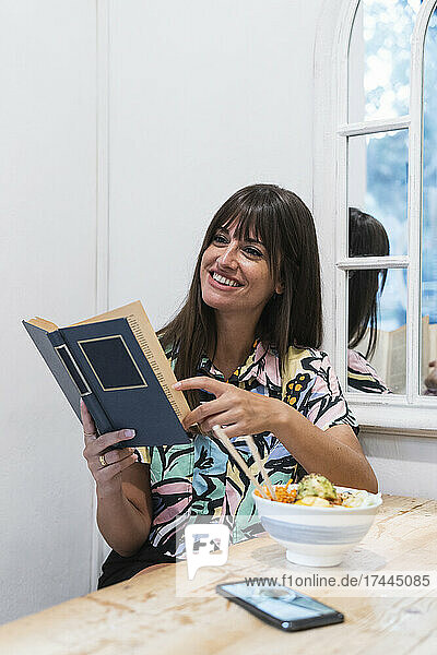 Smiling woman with book sitting at restaurant table