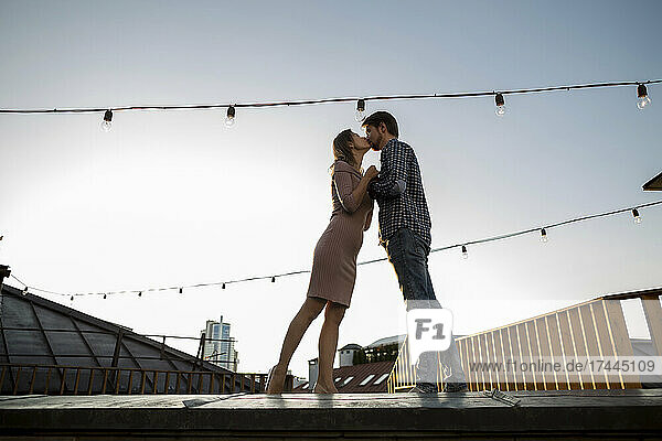 Couple kissing while standing on rooftop during sunset