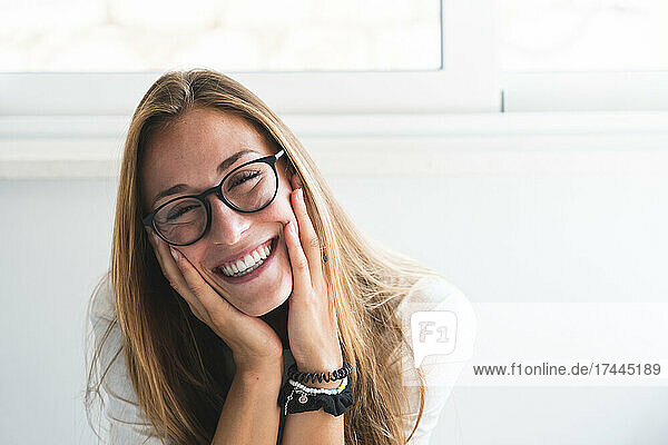 Happy woman wearing eyeglasses sitting with head in hand at home