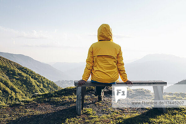 Woman with hooded shirt looking looking at view while sitting on bench
