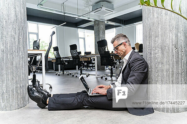 Male business professional using laptop while sitting on floor in office