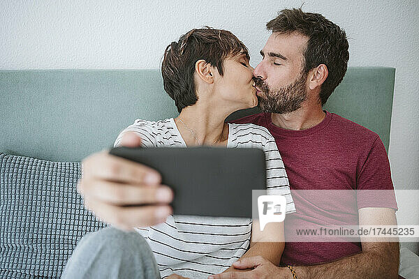 Liebevolles Paar küsst sich  während es zu Hause ein Selfie mit dem Smartphone macht