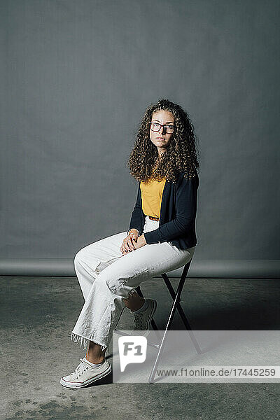 Young woman wearing eyeglasses sitting on chair in studio