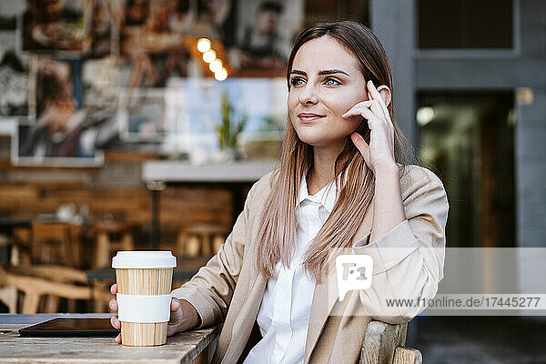Thoughtful businesswoman with disposable cup at coffee shop terrace