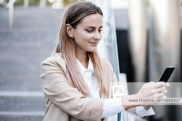 Businesswoman using smart phone while standing at railing