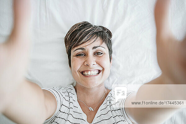 Happy mid adult woman with hands raised lying on bed at home