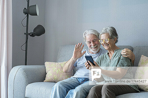 Smiling senior man waving during video call by woman at home