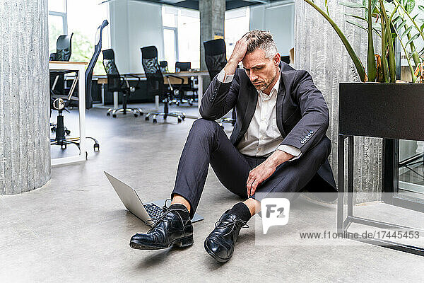 Worried businessman with head in hand sitting on floor in office