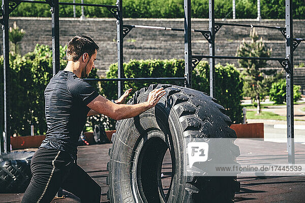 Sportsman exercising with heavy tire during sunny day