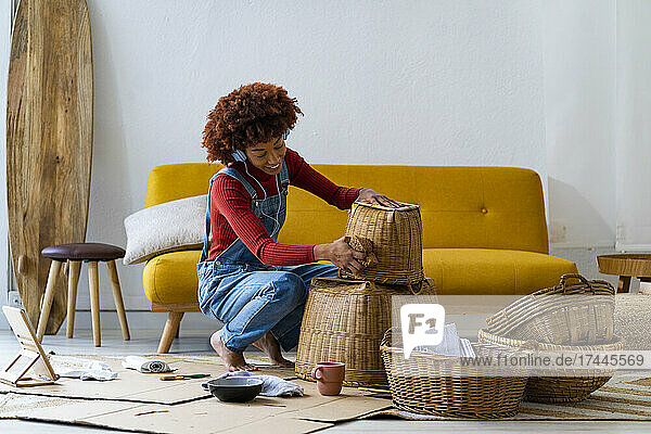 Woman wearing headphones cleaning wicker basket in living room
