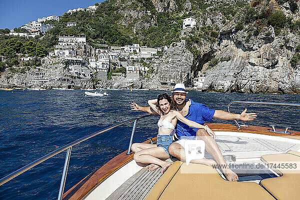 Lächelndes Paar mit ausgestreckten Armen sitzt im Motorboot