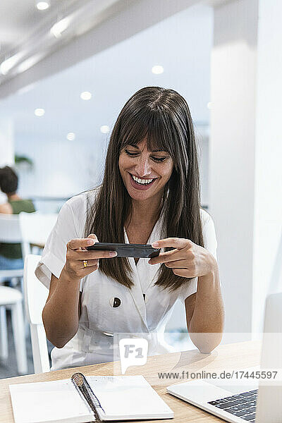 Fröhliche Geschäftsfrau fotografiert ihr Tagebuch per Smartphone im Restaurant