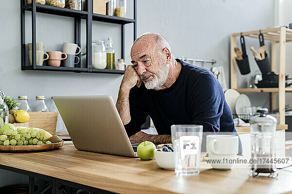 Müder Mann benutzt Laptop am Küchentisch