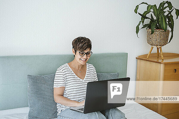 Smiling woman using laptop on bed at home