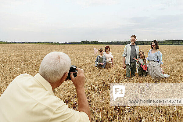 Man photographing family through camera on wheat field