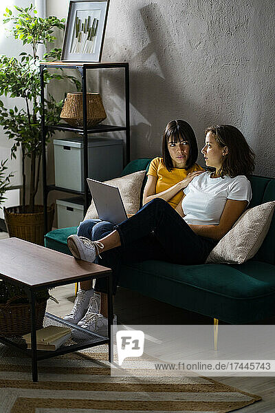 Lesbian couple with laptop talking while sitting on sofa at home