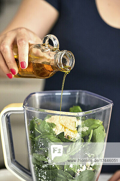 Pouring olive oil in food processor  making basil and arugula pesto