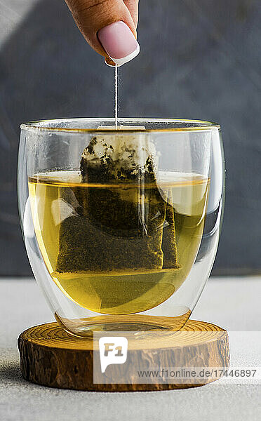 Frau hält Teebeutel mit grünem Tee in Teeglas