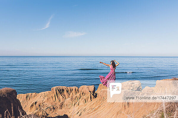 Woman wearing a pink dress on a cliff with the ocean in the back