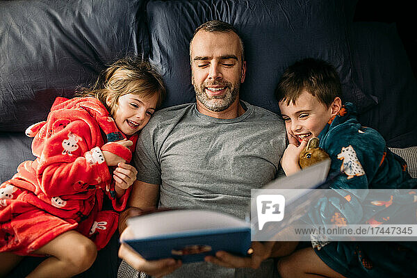 Father reading a book to his children in the master bedroom at night