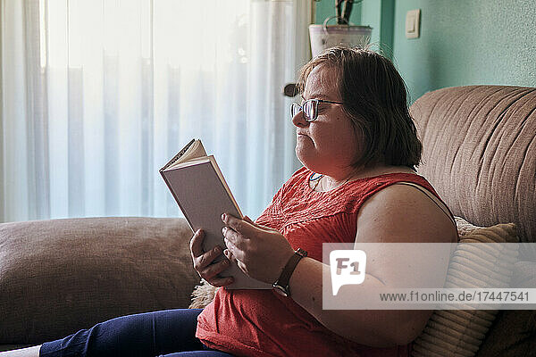 Down syndrome woman reads a book on the couch at home