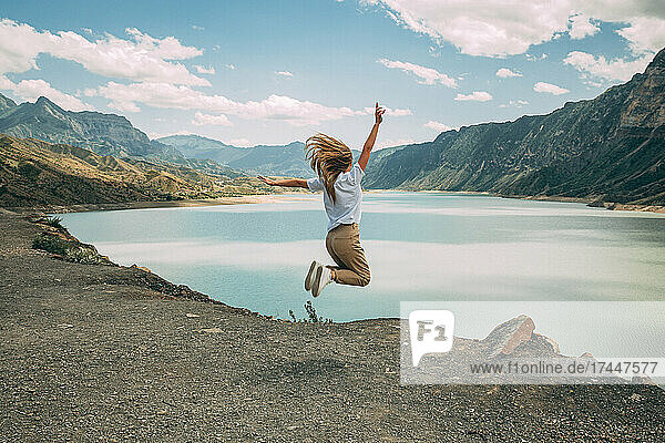 The girl full of joy jumps against the background of mountains