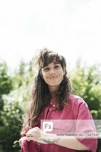 Portrait of smiling woman pink shirt cleaning glasses outside in sun