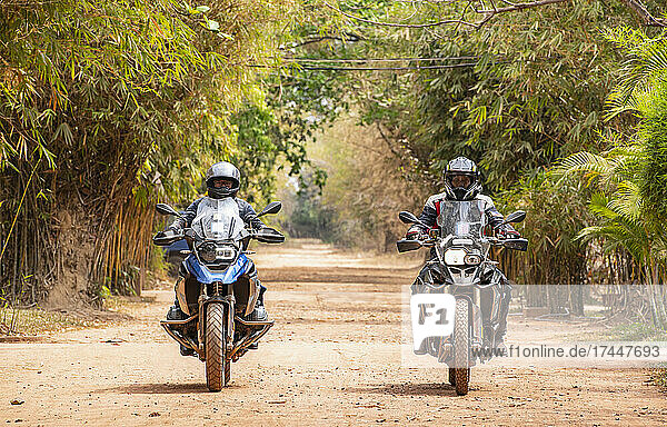 Two men riding their adventure motorbike on dirt road in Cambodia