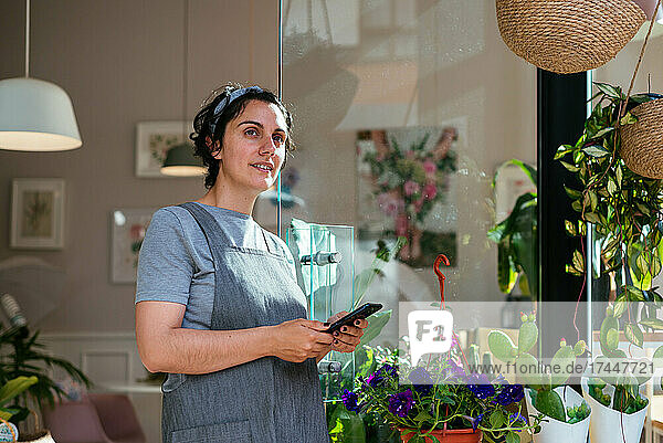 Florist standing at the door of her flower shop using a smartphone