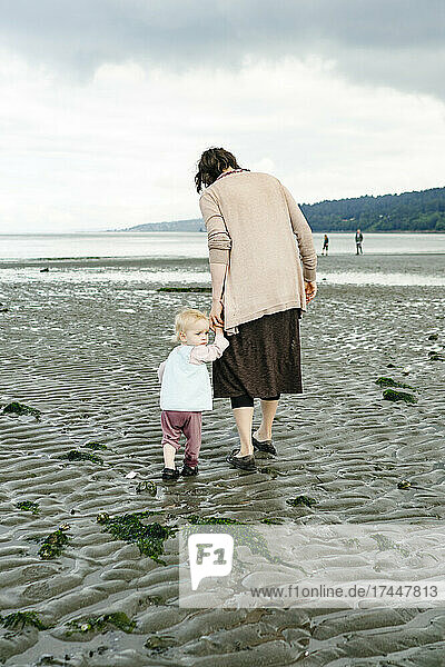 A young girl looking back while holding her mother's hand on the beach