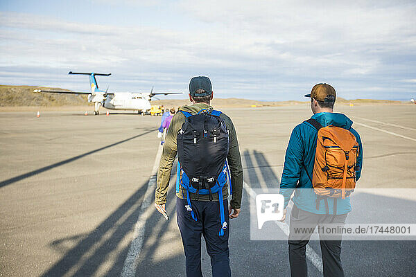 Rear view of two backpackers walking on tarmac towards an airplane