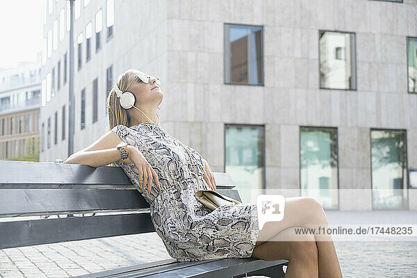 young woman sitting on a bench and listening musik with headphones