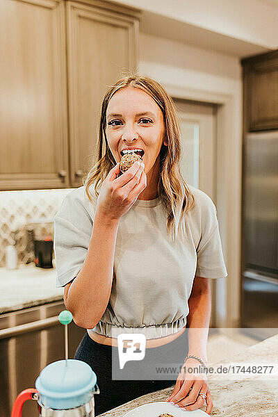 Smiling woman eats protein bite in her kitchen