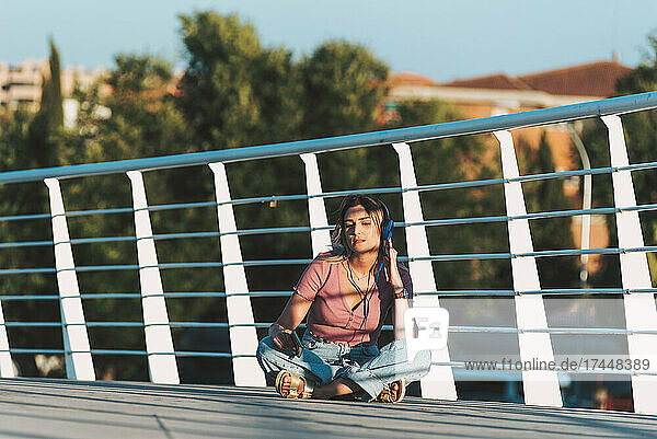 Woman sitting on a bridge listening to music.