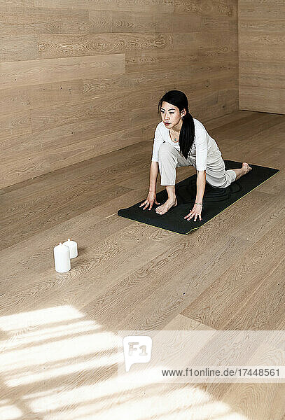 Young concentrated woman doing yoga exercises while sitting on floor