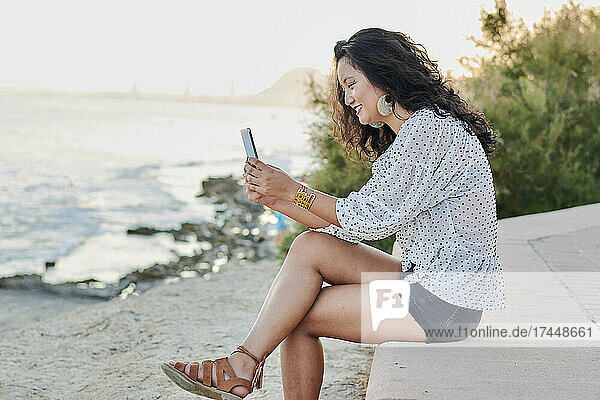 Young Asian woman looks her smartphone with the sea on the background