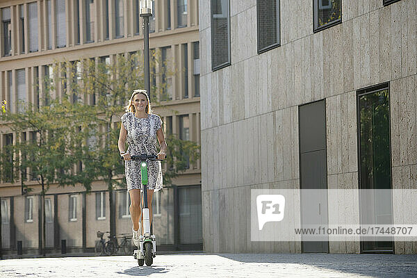 Young woman riding e-scooter in city in summer