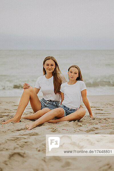 two teenager girls sitting on the beach by the sea
