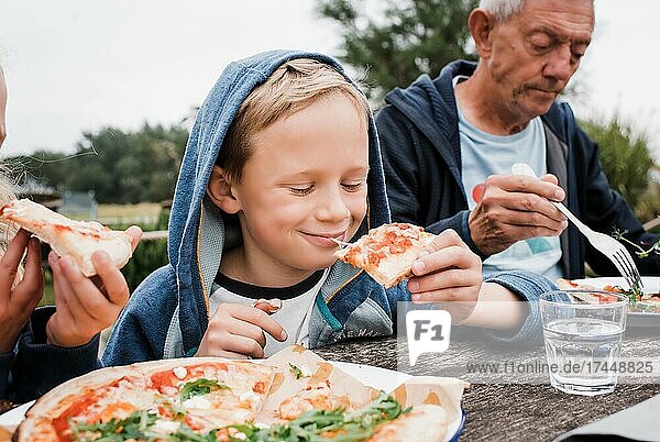 boy happily eating pizza with his family outside in the garden