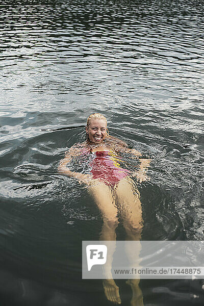 Smiling blond woman in colourful swimsuit swimming in lake in summer