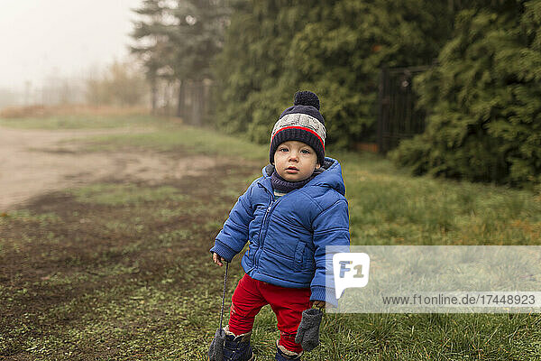 Small boy standing on grass in winter clothes in foggy weather