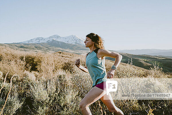 A woman trail runs through a field in golden light with mountain view