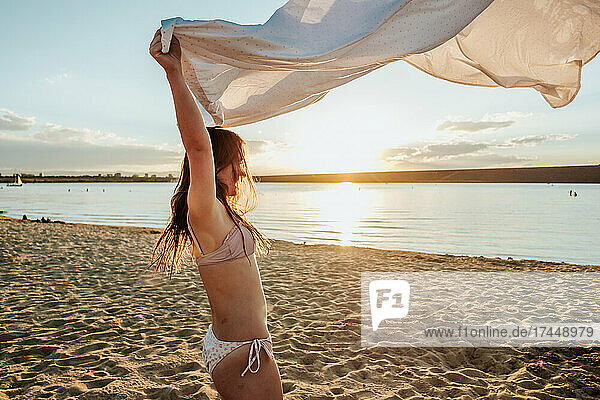 Teen girl playing with white sheet at sunset on the beach