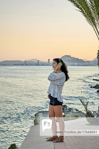 Young Asian woman listens to music with the sea in the background