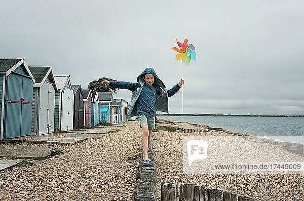 boy balancing on a wall at the beach playing with a windmill