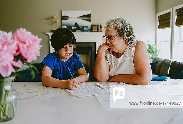 Grandmother helping grandson with writing homework at home.