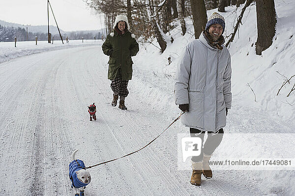 women laugh walking dogs in snow jackets in frozen winter country road