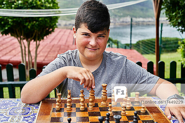 Young boy looking at camera sitting behind the chessboard.