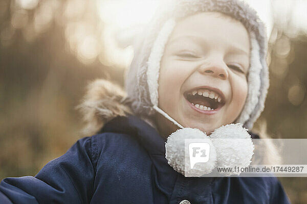Head of small boy laughing in the forest in winter hat