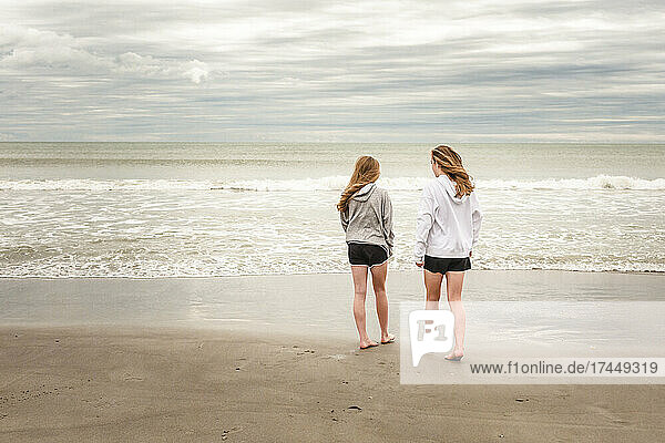 Teen girls in hoodies walk on deserted Florida beach in winter